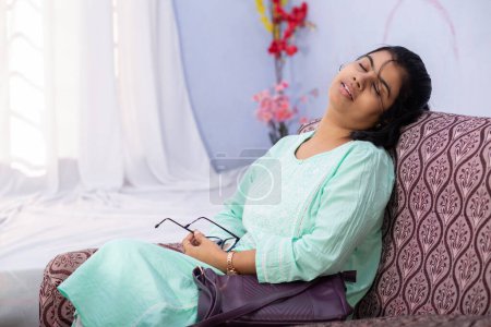 Una mujer india descansando en un sofá con sus gafas en la mano regresando del trabajo