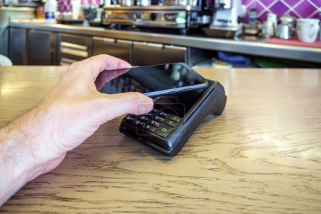 Téléchargez les photos : Un client restaurant utilisant un smartphone pour payer dans un terminal de paiement. Tpv. - en image libre de droit
