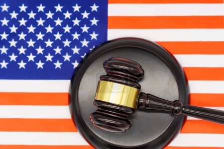Justice Under the Stars and Stripes. Un mazo de jueces descansa en un bloque de sonido contra el telón de fondo de una bandera estadounidense, simbolizando la ley y el orden en los Estados Unidos.