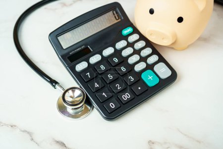 Una alcancía con una calculadora y estetoscopio muestra el aspecto financiero de la atención médica.