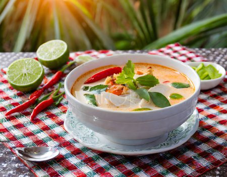 Foto de Sopa tailandesa aromática Tom Kha kai con leche de coco, limoncillo y pollo presentado en una mesa rústica con lima y chiles - Imagen libre de derechos