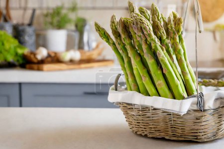 Una cesta llena de espárragos verdes se sienta en un mostrador de cocina con un fondo borroso, destacando la alimentación saludable y la cocina en casa