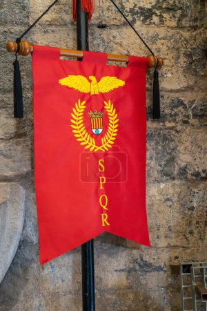 Photo for Red banner in vertical view with a symbol of ancient Rome, consisting of an eagle and a laurel wreath and the legend SPQR. Senatus Populus que Romanus - Royalty Free Image
