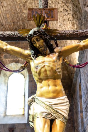 Téléchargez les photos : Une statue de Jésus-Christ tient une croix dans ses mains. La croix est ornée de perles rouges et la statue est entourée de fleurs. Concept de révérence et de spiritualité - en image libre de droit