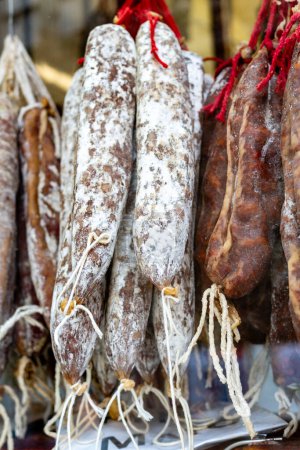 Téléchargez les photos : Salami espagnol, fuet et saucisses de salchichn accrochés sur une étagère sur un fond noir - en image libre de droit