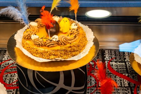 Photo for A mona de pascua, a cake eaten in Spain on Easter Monday, topped with a chocolate chick, on a rustic wooden surface full of decorated eggs and feathers of different colors - Royalty Free Image