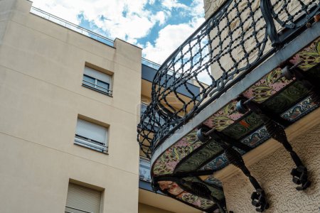 La imagen muestra la yuxtaposición de la arquitectura lisa moderna con un intrincado balcón antiguo, destacando el contraste en estilos
