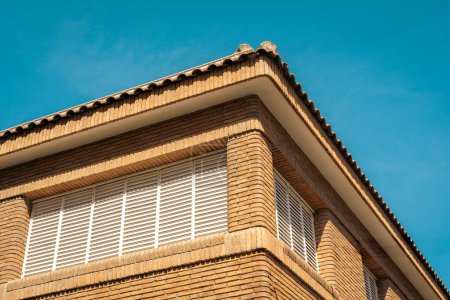 Foto de Fachada de edificio modernista bajo cielo azul claro con detalles arquitectónicos y persianas venecianas - Imagen libre de derechos