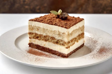 Ein klassisches italienisches Dessert, Tiramisu, präsentiert auf einem weißen Teller mit sichtbaren Schichten und mit Kakao bestäubt, was auf ein genussvolles Geschmackserlebnis hindeutet