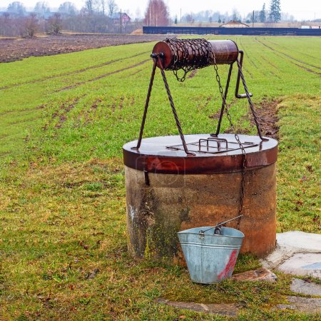 Ein alter Brunnen mit Metallabdeckung und Walze, ein Eimer zum Auffangen des Wassers im Frühling