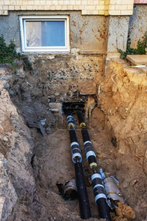 Photo for In the spring, new heat-insulating water pipes are laid in the trench near the foundation of the house - Royalty Free Image