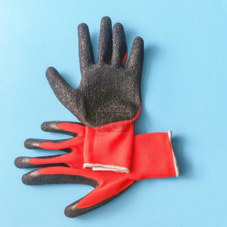Photo for Top view of knitted red gloves with black latex covered palms on blue background - Royalty Free Image