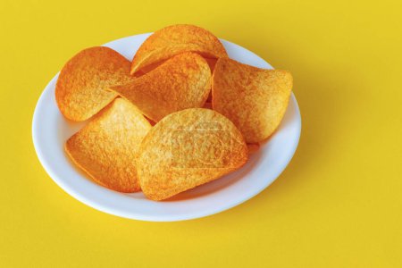 Top view of round crispy potato chips with paprika on a plate on a yellow background