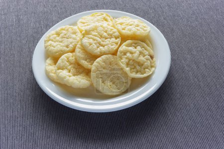 Lots of round rice chips with cheese flavor on a plate, gray wooden tablecloth on the table