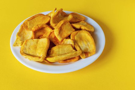 Image of round crispy potato chips with paprika on a white plate on a yellow background