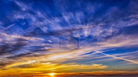 Una puesta de sol con tonos vibrantes de azul, naranja y amarillo como nubes tenues rodar sobre la tranquila línea del horizonte. El contraste de colores cálidos y fríos crea un final dinámico y pacífico al día.