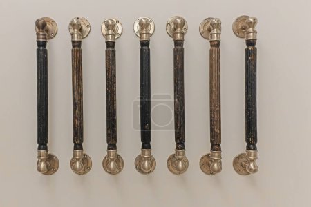 A collection of vintage walking sticks, each with a uniquely designed handle, are neatly lined up against a plain, light wall. Characterized by various textures and patterns
