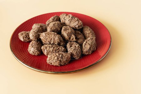 Chocolate truffles covered with milk chocolate chips on red plate on orange background front view