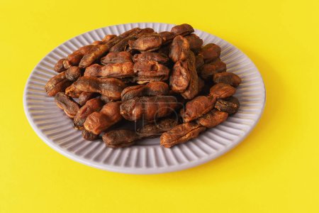Sweet spicy tamarind tree fruit pulp on plate on yellow background close up