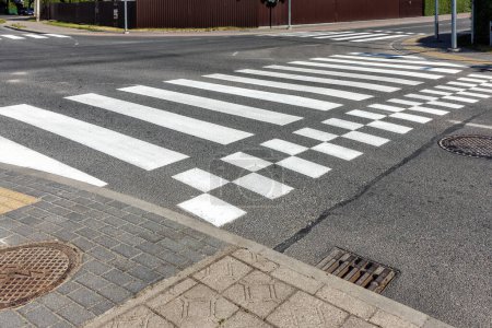 The white-striped crosswalk is empty, the sunlight creating a contrast on the asphalt, and the lack of pedestrians or traffic indicating early morning.
