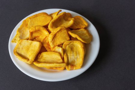 Téléchargez les photos : Keripik Sukun ou chips de fruits à pain est un aliment à base de fruits à pain qui est finement tranché et frit jusqu'à ce que sec et croustillant. Servi sur une assiette blanche sur un fond sombre - en image libre de droit