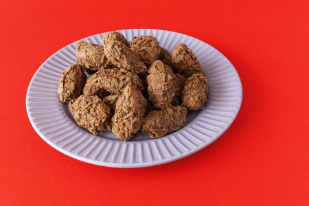 Belgian chocolate truffles covered with milk chocolate chips on a plate on a red background front view