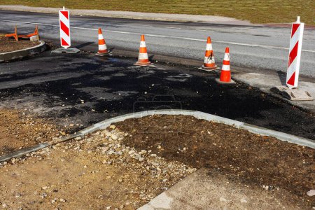 Un camino de asfalto con una serie de conos de tráfico naranja y blanco colocados esporádicamente a lo largo de su longitud. Los conos se utilizan para marcar secciones, carriles, o indicar trabajos de carretera o peligros.