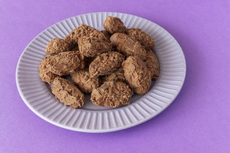 Belgian chocolate truffles covered with milk chocolate chips on a plate on a purple background, front view