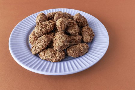 Belgian chocolate truffles covered with milk chocolate chips on a plate on a brown background, front view