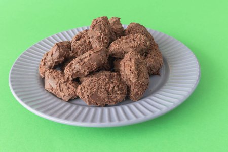 Belgian chocolate truffles covered with milk chocolate chips on a plate on a green background, front view