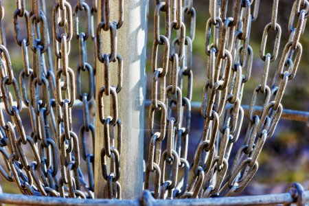 A close-up reveals the intricate network of metal chains hanging from a disc golf basket, designed to catch frisbees in the sport.