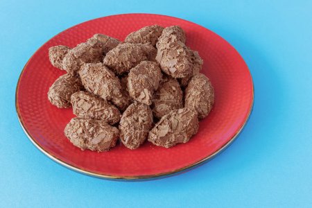 Belgian chocolate truffles covered with milk chocolate chips on a red plate on a blue background.