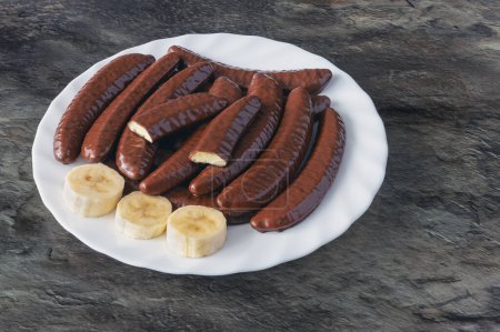 Banana flavored slices covered with chocolate on a white plate on a marble table surface