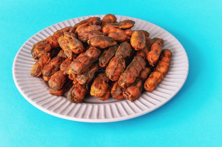 Top view of sweet spicy tamarind tree fruit pulp in round plate on blue background