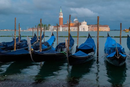 Photo for Gondolas rest parked along the Grand Canal  for the evening with the Church of San Giorgio in. the background - Royalty Free Image