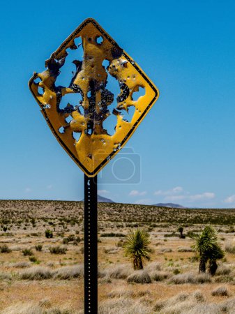 A traffic sign is riddled with bullet holes as it stands along a rural desert road