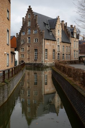 Foto de The Demer river and the 16th century building 'Het Spijker' (also known as Hof van Tongerlo) in the Flemish Brabant city of Diest, in Belgium. Winter view with reflections in the water. - Imagen libre de derechos