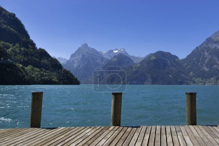 View across the arm of Lake Lucerne known as Urnersee or Lake Uri, in Uri, Switzerland. Summer day with a view of the Swiss alp mountains from Sisikon, with blue sky and blue-green water. Copyspace.