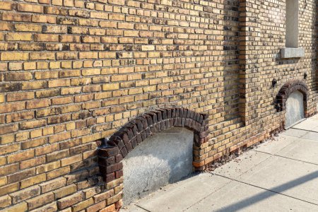 Foto de Fondo de textura de marco completo de una antigua pared de ladrillo exterior de color amarillo y marrón moteado chic, con vista a una ventana cerrada del sótano arqueada - Imagen libre de derechos