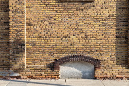 Foto de Fondo de textura de marco completo de una antigua pared de ladrillo exterior de color amarillo y marrón moteado chic, con vista a una ventana cerrada del sótano arqueada - Imagen libre de derechos