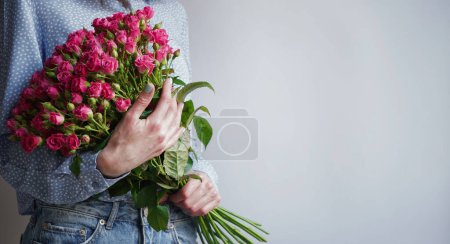 International Women's Day.Concept of greeting banner for international women's day on March 8.Close-up of girl's hands holding gift box and large bouquet of pink roses on gray background,copy space