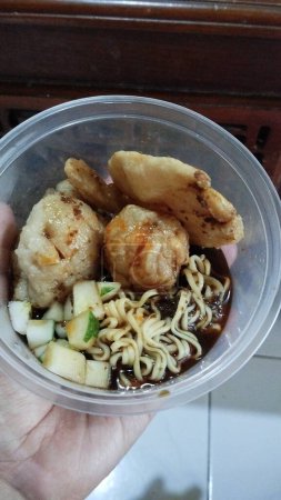 Photo for Fried noodles with fish balls in a plastic container on hand. Pempek in a bowl with typical Indonesian Palembang vinegar sauce. Indonesian traditional food. local wisdom - Royalty Free Image
