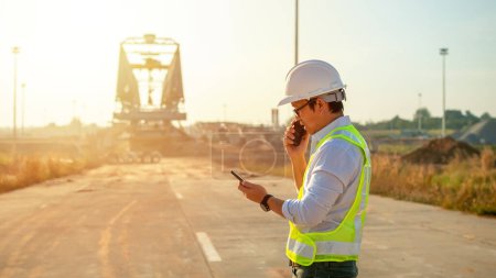 Foto de Engineer talking on walkie-talkie and using smart phone for working at construction site - Imagen libre de derechos