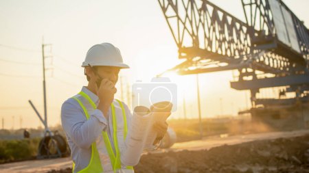 Photo for Men Engineer talking on walkie-talkie and holding blueprint for inspecting and working at construction site - Royalty Free Image