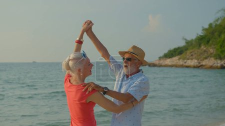 Téléchargez les photos : Deux hommes et femmes âgés dansant à la plage pendant leurs vacances d'été et ils sourient et profitent de leur journée de congé. - en image libre de droit