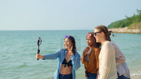 Téléchargez les photos : Un groupe de jeunes femmes utilisant des téléphones portables pour prendre des selfies à la plage pendant leurs vacances d'été et ils sourient et profitent de leurs vacances. - en image libre de droit