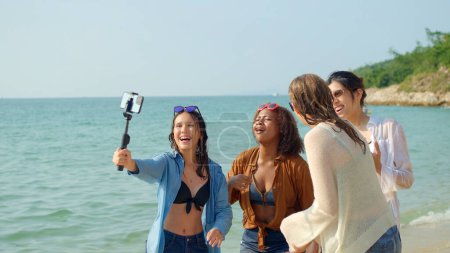Photo for A group of young women using mobile phones to take selfies at the beach on their summer vacation and they smile and enjoy their vacation. - Royalty Free Image