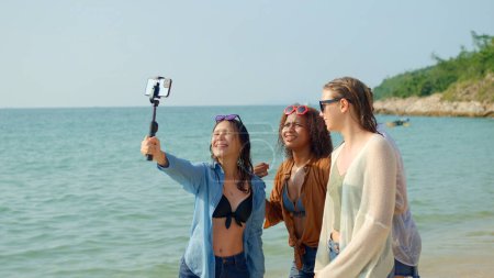 Photo for A group of young women using mobile phones to take selfies at the beach on their summer vacation and they smile and enjoy their vacation. - Royalty Free Image
