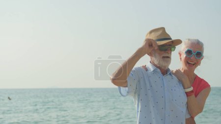 Téléchargez les photos : Un couple de personnes âgées serre leurs épaules à la plage pendant leurs vacances d'été et ils sourient et profitent de leurs vacances. - en image libre de droit