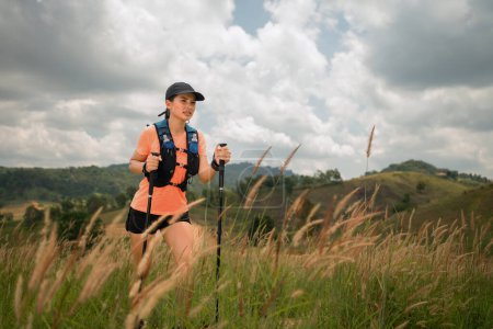 Téléchargez les photos : Young women active trail running across a meadow on a grassy trail high in the mountains in the afternoon with trekking pole - en image libre de droit